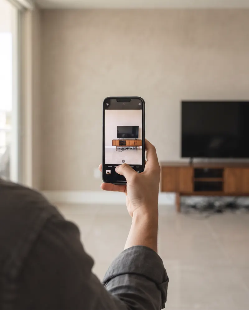 A hand photographing a plain wall with an old TV stand and loose cables
